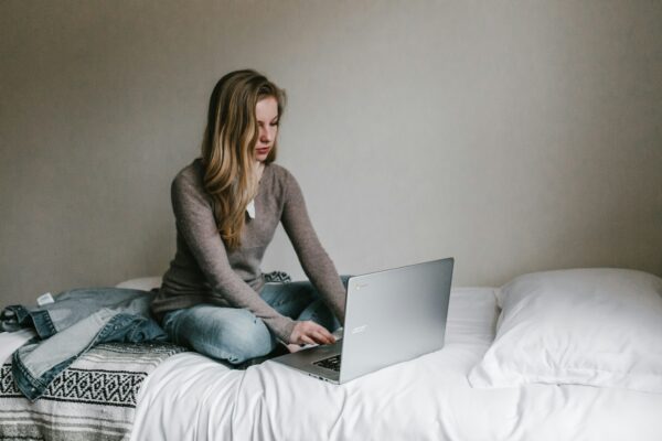 woman typing on MacBook Pro while sitting on bed in room