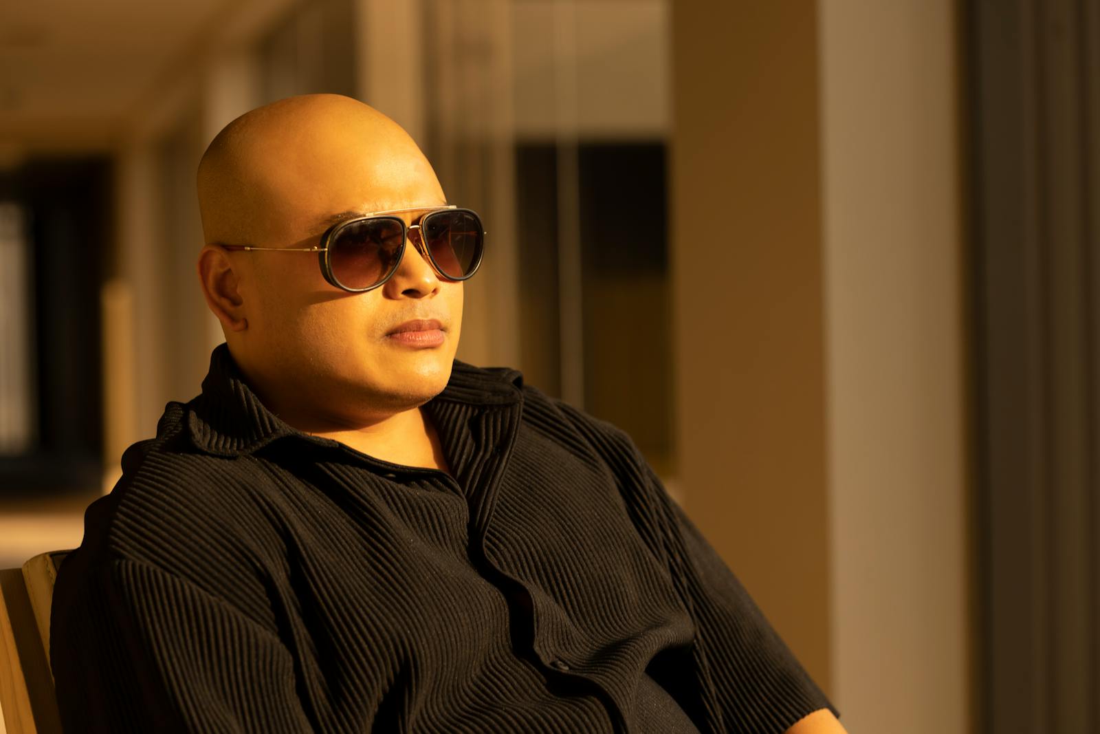 A bald man in sunglasses sits in thoughtful repose, bathed in warm sunlight.