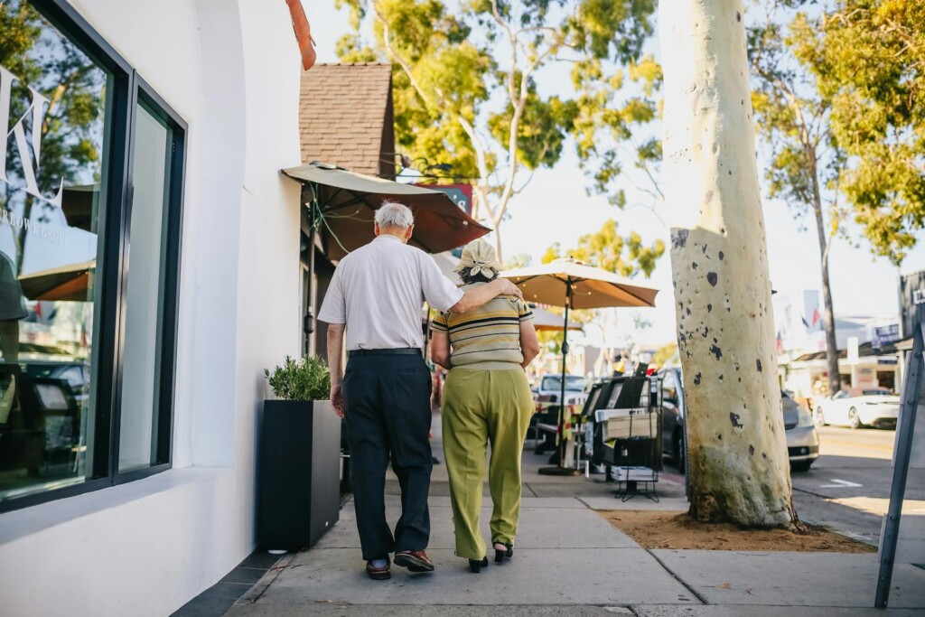A senior couple walking closely on a sunny city street, embracing the outdoors together.